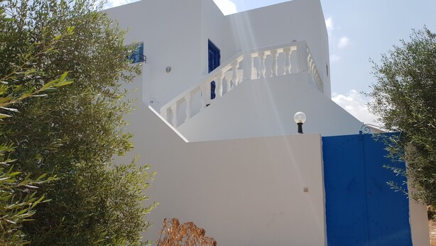 Een modern gebouw met een witte gevel, een blauwe poort en een trap die naar een hoger gelegen niveau leidt.