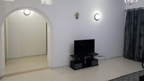 Een woonkamer met een televisie op een zwart dressoir, een plafondlamp en een zwart gordijn.