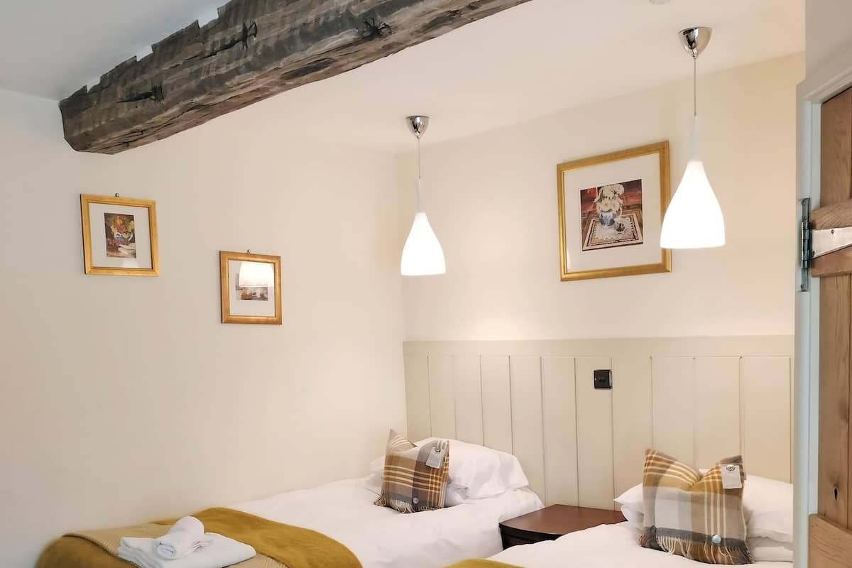 Ein Hotelzimmer mit zwei Betten, jeweils mit einer braunen Decke und einem weißen Kopfkissen. An der Wand hängen zwei gerahmte Bilder, eine Deckenleuchte und ein Holzbalken.