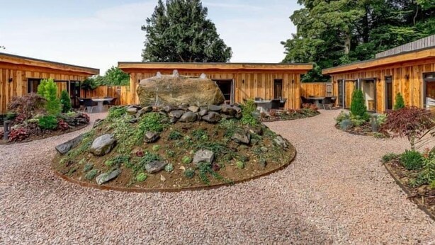 A modern building with a central courtyard featuring a rock formation and surrounding greenery. - Cann Office Hotel (Welshpool)