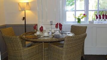 Una mesa de comedor con sillas de mimbre, una lámpara y una ventana con flores.
