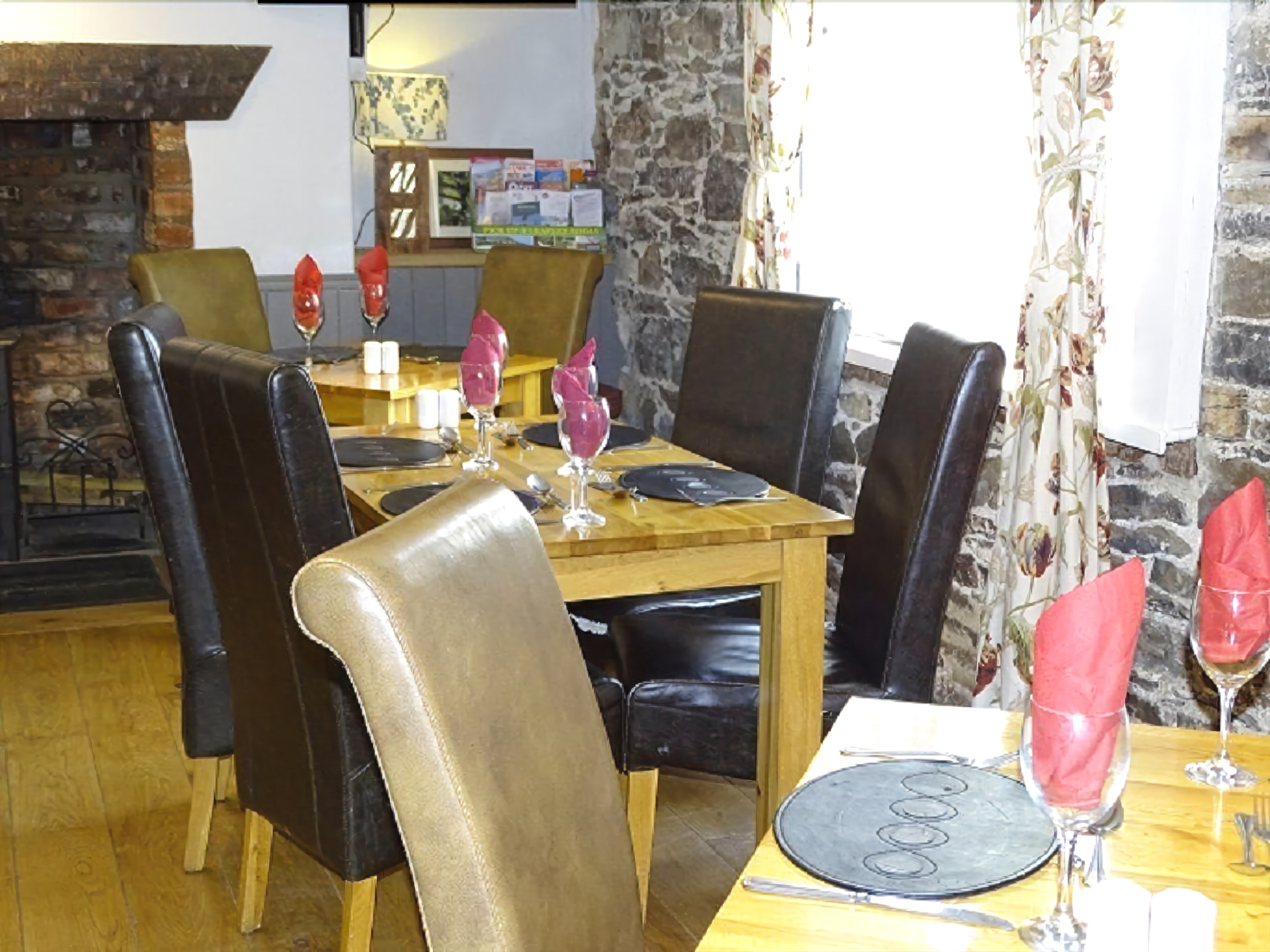 Un comedor con una mesa de madera dispuesta para cuatro personas, rodeada de sillas de cuero. Se observa una pared de piedra y una chimenea al fondo.