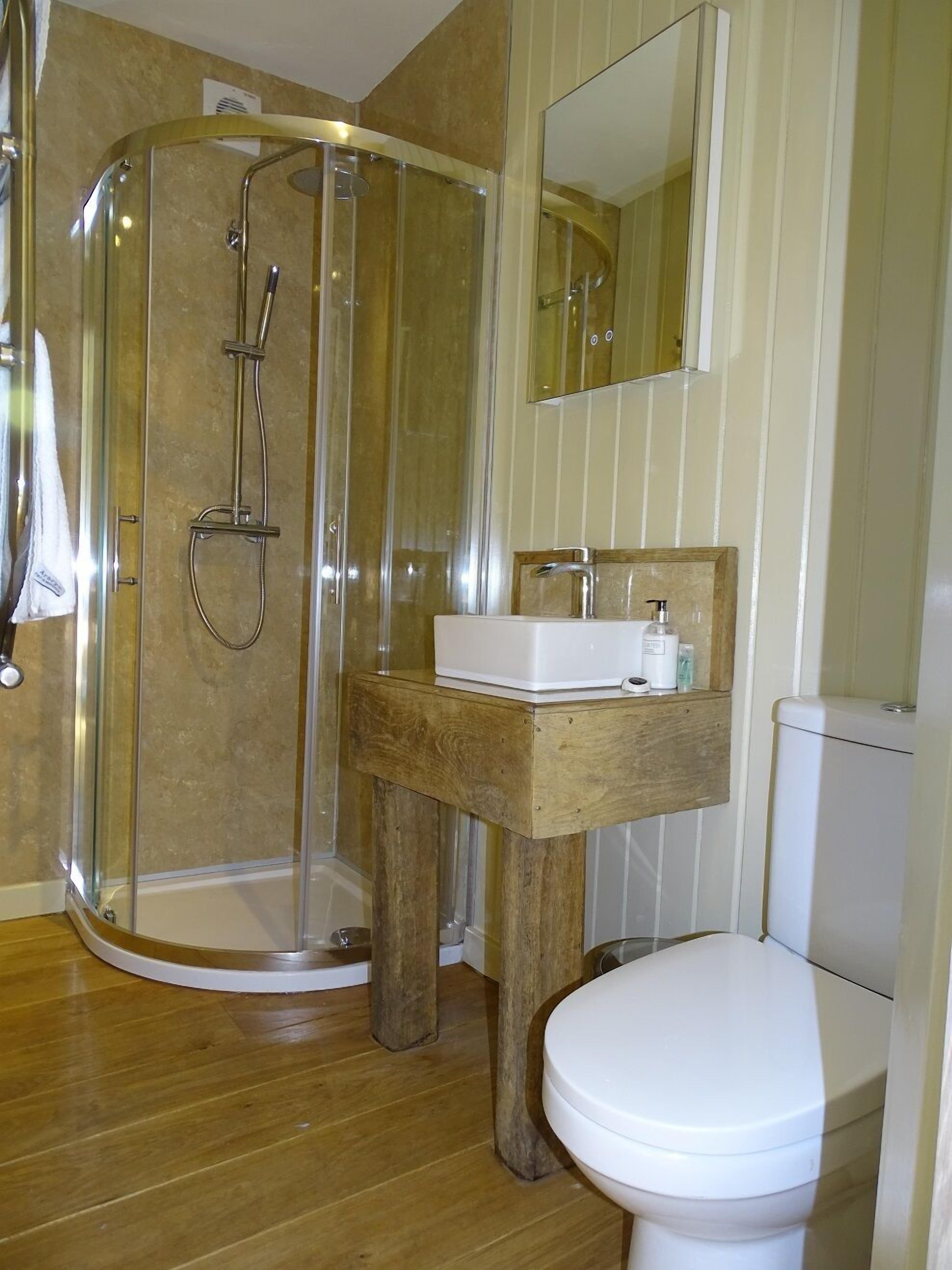 A bathroom with a glass-enclosed shower, a wooden vanity, and a white toilet.