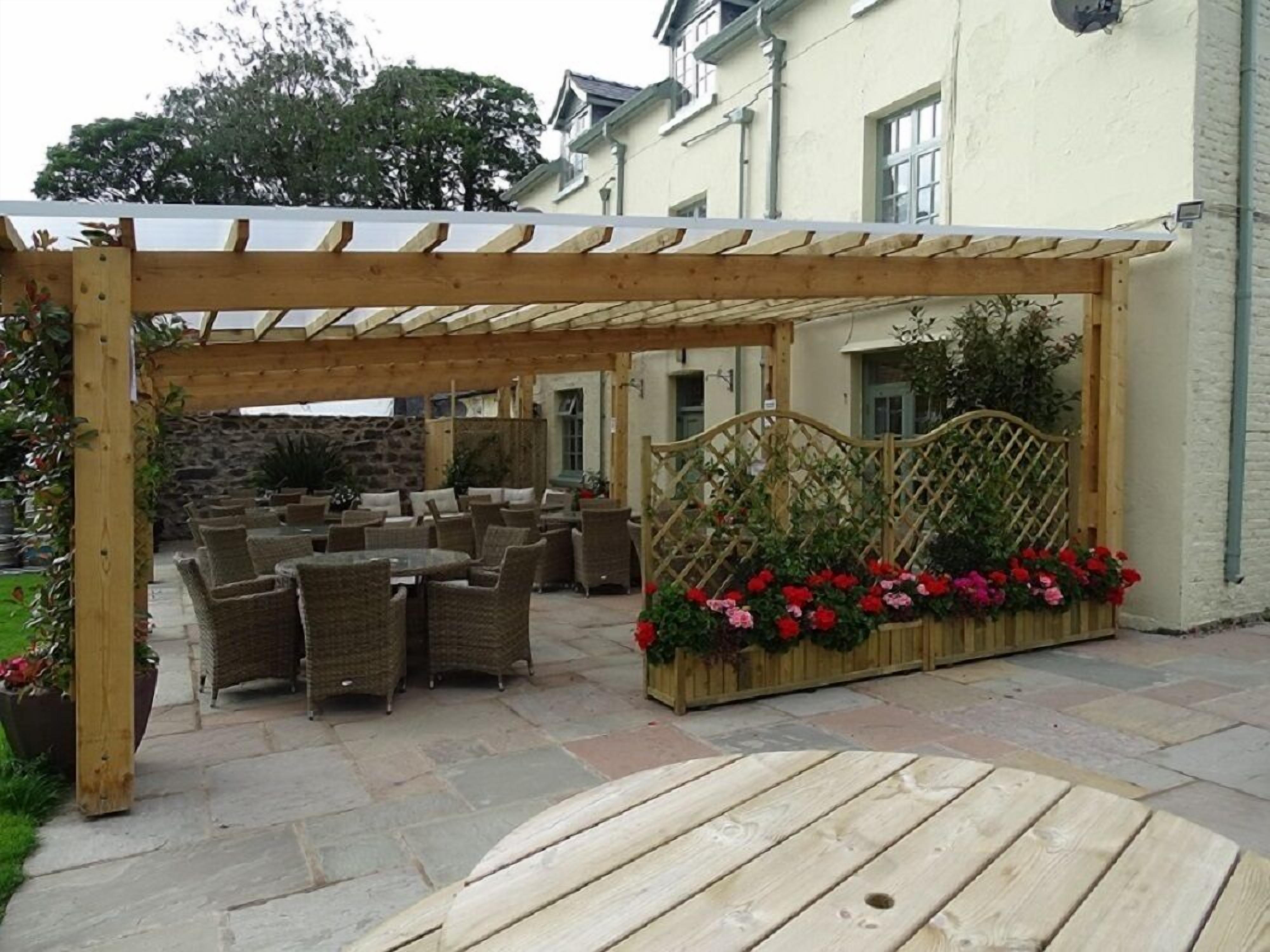 Een terras buiten met rieten meubilair en een houten pergola.