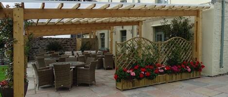 Een terras buiten met rieten meubilair en een houten pergola.
