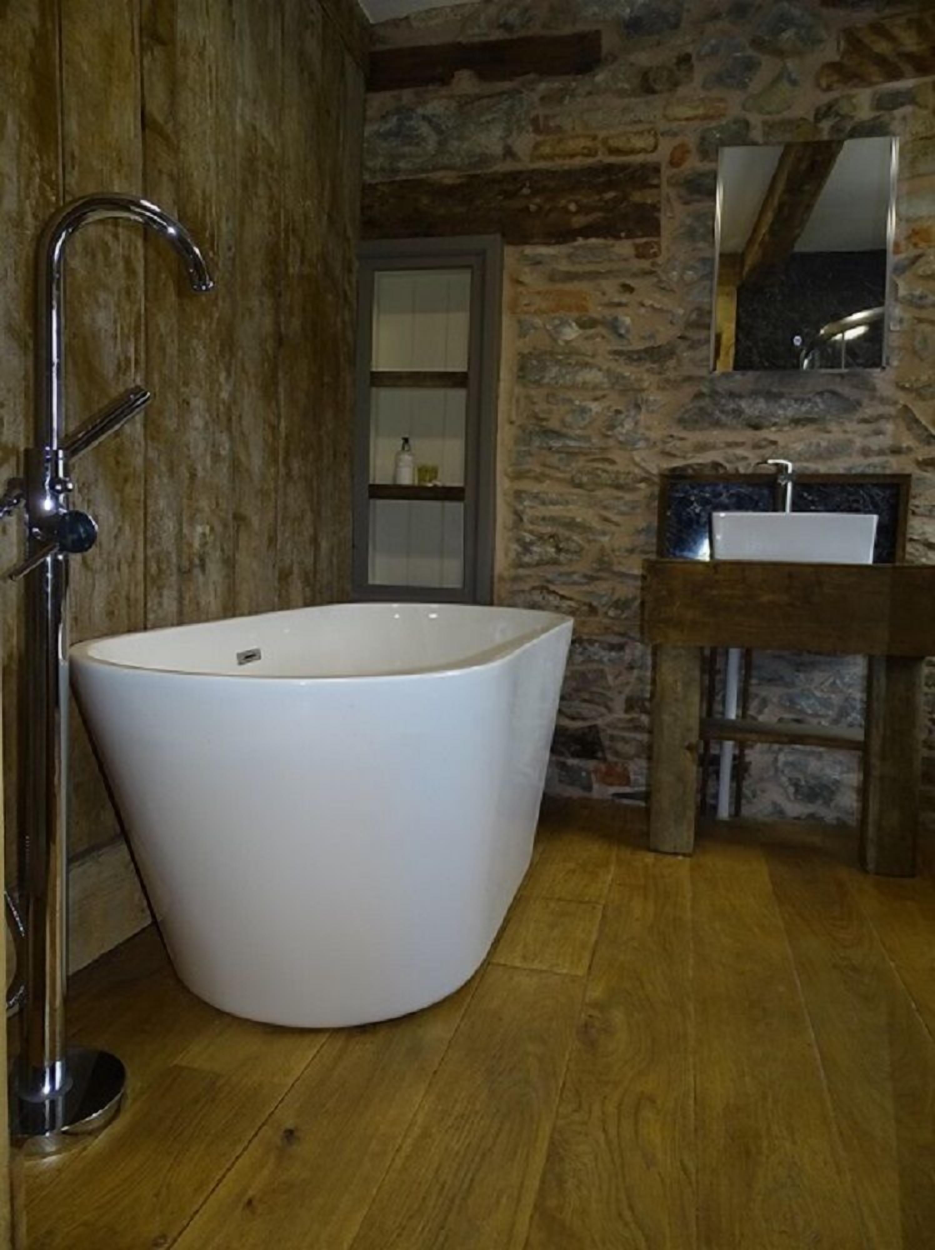 Un baño con una bañera independiente, un tocador de madera y una pared de piedra.