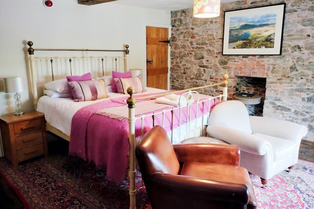 Ein Schlafzimmer mit Bett, Nachttisch, Stuhl, Kamin und Steinwand.