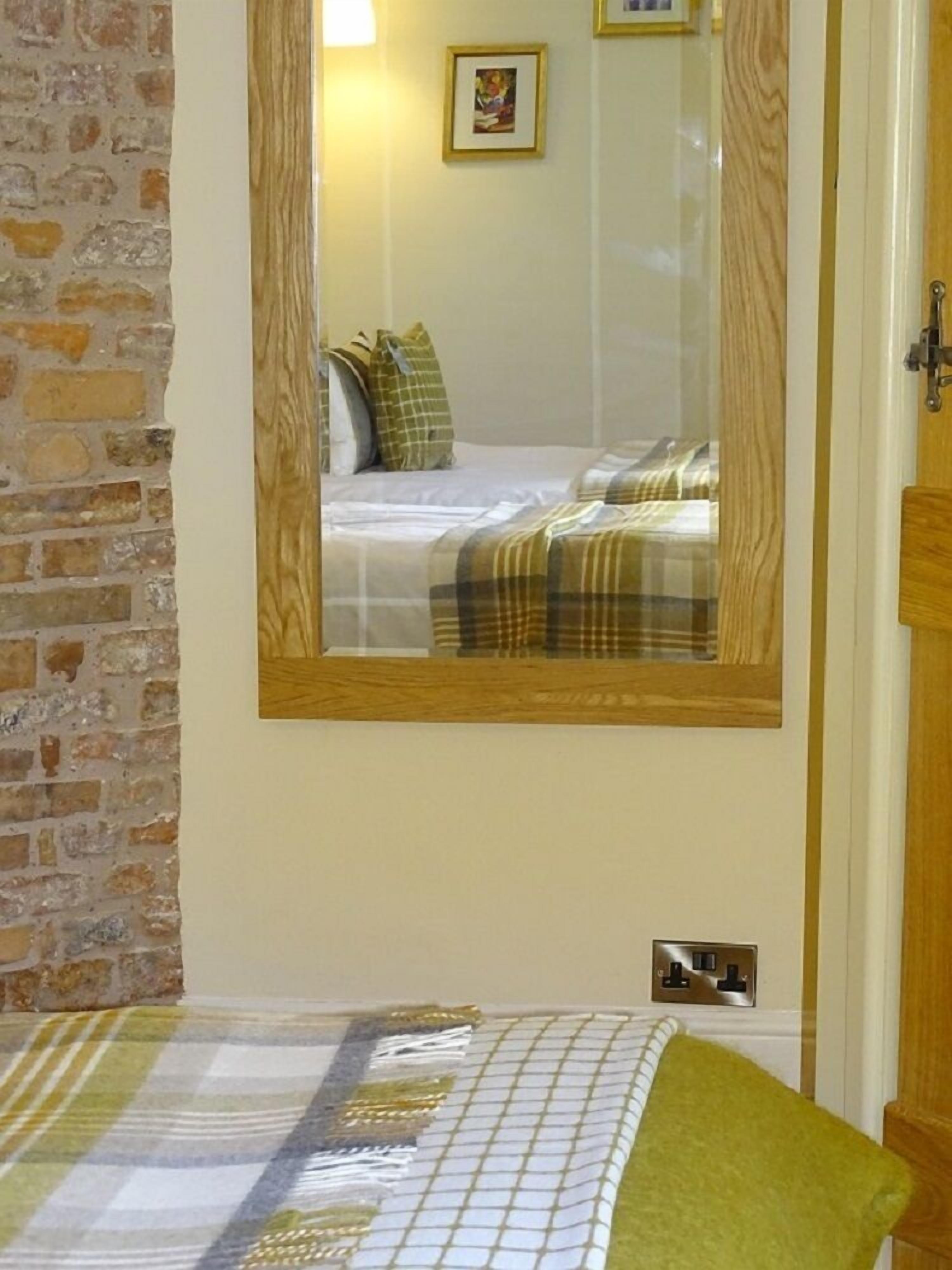 A bedroom with a bed, a mirror, a brick wall, and a wooden door.