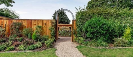 Un sendero de jardín que conduce a una puerta de madera con un arco de metal.
