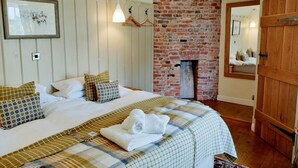 A bedroom with a bed, a hanging light, a brick wall, and a wooden door. - Cann Office Hotel (Welshpool)