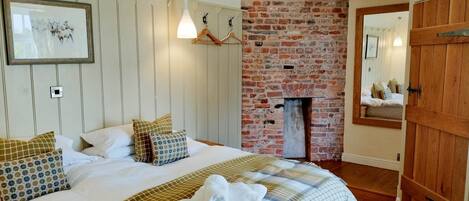 A bedroom with a bed, a hanging light, a brick wall, and a wooden door.