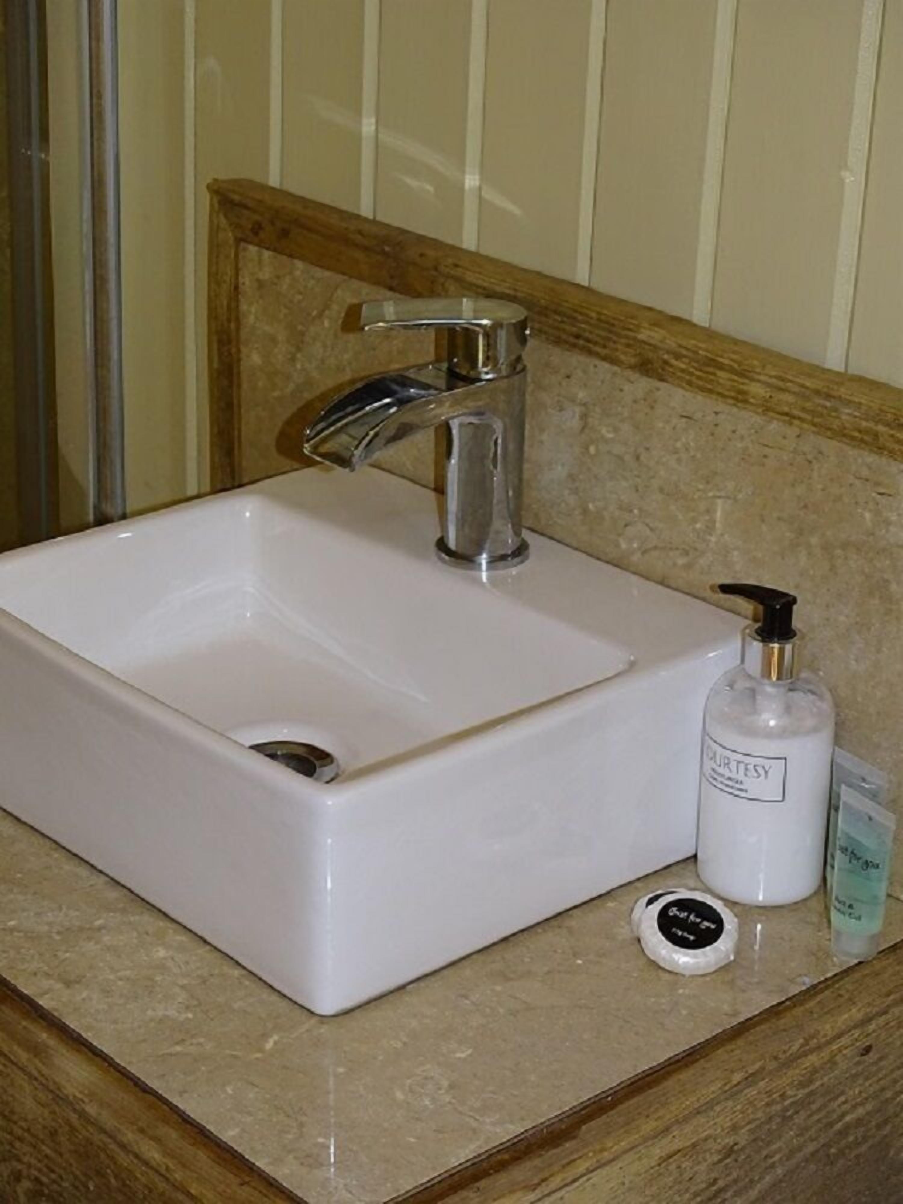 A bathroom sink with a chrome faucet, a white bottle of Courtesy soap, and a small round soap dish.
