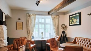 A cozy room with leather furniture, a round table, and a window with curtains. - Cann Office Hotel (Welshpool)