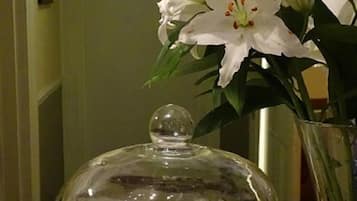 Una mesa con una cúpula de vidrio que muestra pasteles, un jarrón con flores blancas y un mantel individual con estampado blanco y negro.