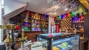 A bar area with shelves of liquor bottles, a Coca-Cola refrigerator, a glass display case with fruits, and a calendar on the counter. - Hotel Sapana Garden (Kathmandu)