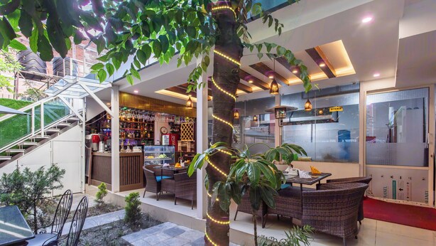 A modern outdoor dining area with wicker furniture, a staircase leading to an upper level, and a bar area visible through glass doors. - Hotel Sapana Garden (Kathmandu)