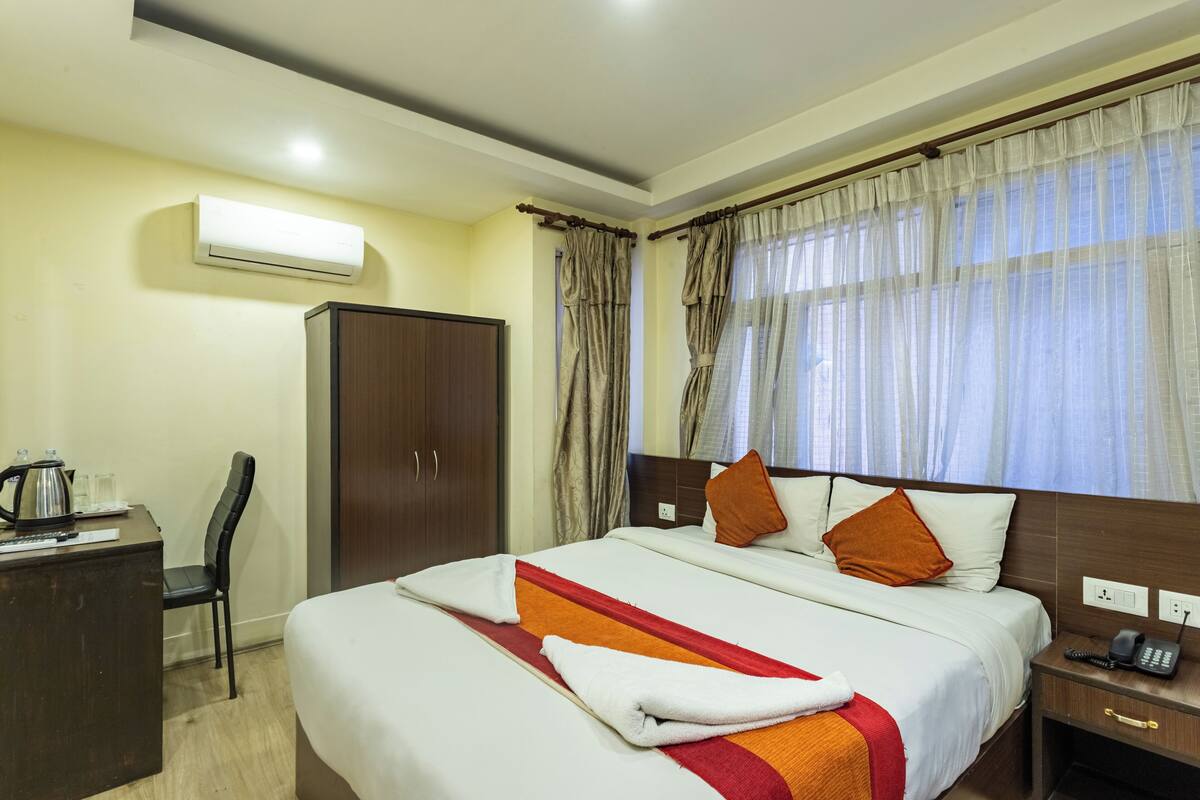 Ein Hotelzimmer mit einem Bett, einem Schreibtisch mit Wasserkocher, einem Kleiderschrank und einem Fenster mit Vorhängen.