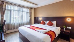 A hotel room with a large bed, a nightstand, a wall-mounted light, and a window with curtains. - Hotel Sapana Garden (Kathmandu)