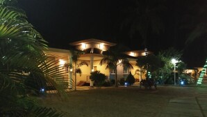 A well-lit hotel with a central courtyard, palm trees, and a staircase leading to the entrance.