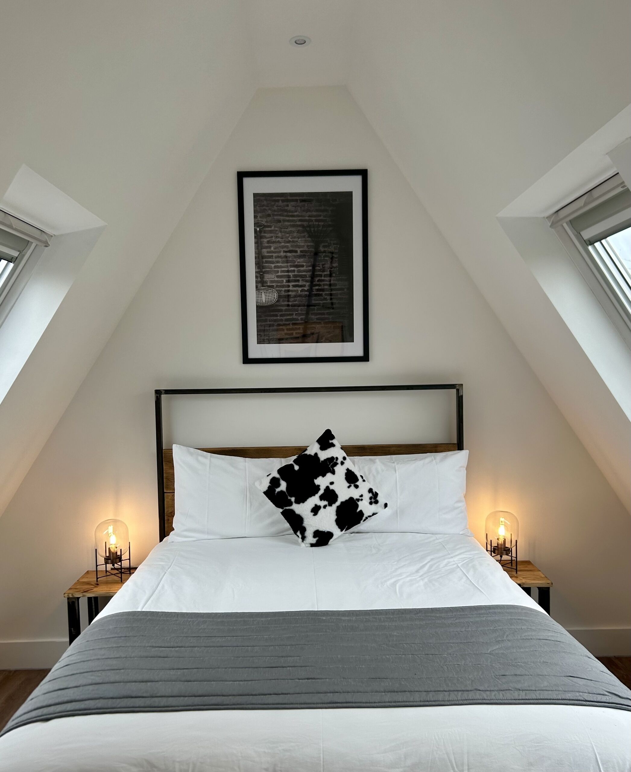 A bedroom with a bed, a framed picture on the wall, and two bedside lamps.