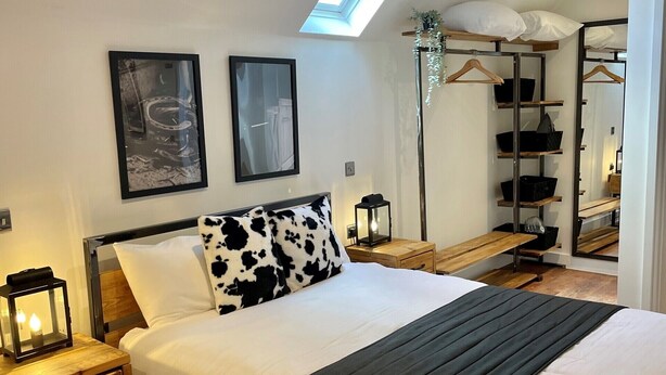 Une chambre moderne avec un grand lit, des tables de chevet en bois, une lucarne et un dressing avec des étagères.