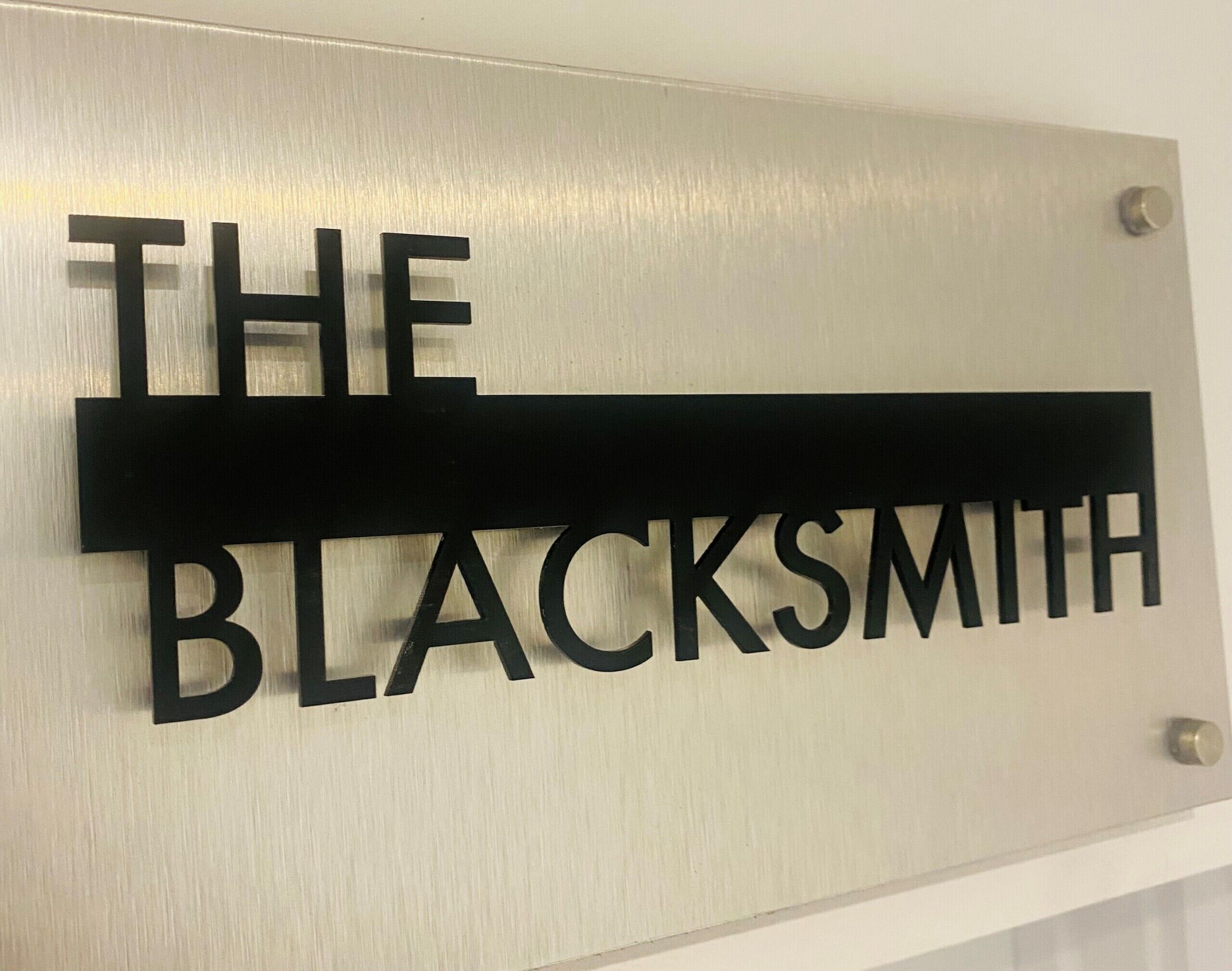Ein metallisches Schild mit der Aufschrift 'THE BLACKSMITH' an einer Wand befestigt.