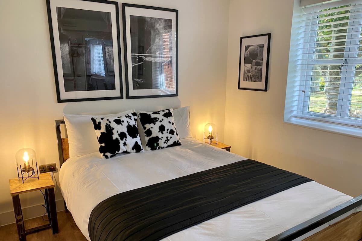A neatly made bed with a black and white striped blanket, two bedside tables with lamps, and framed pictures on the wall.