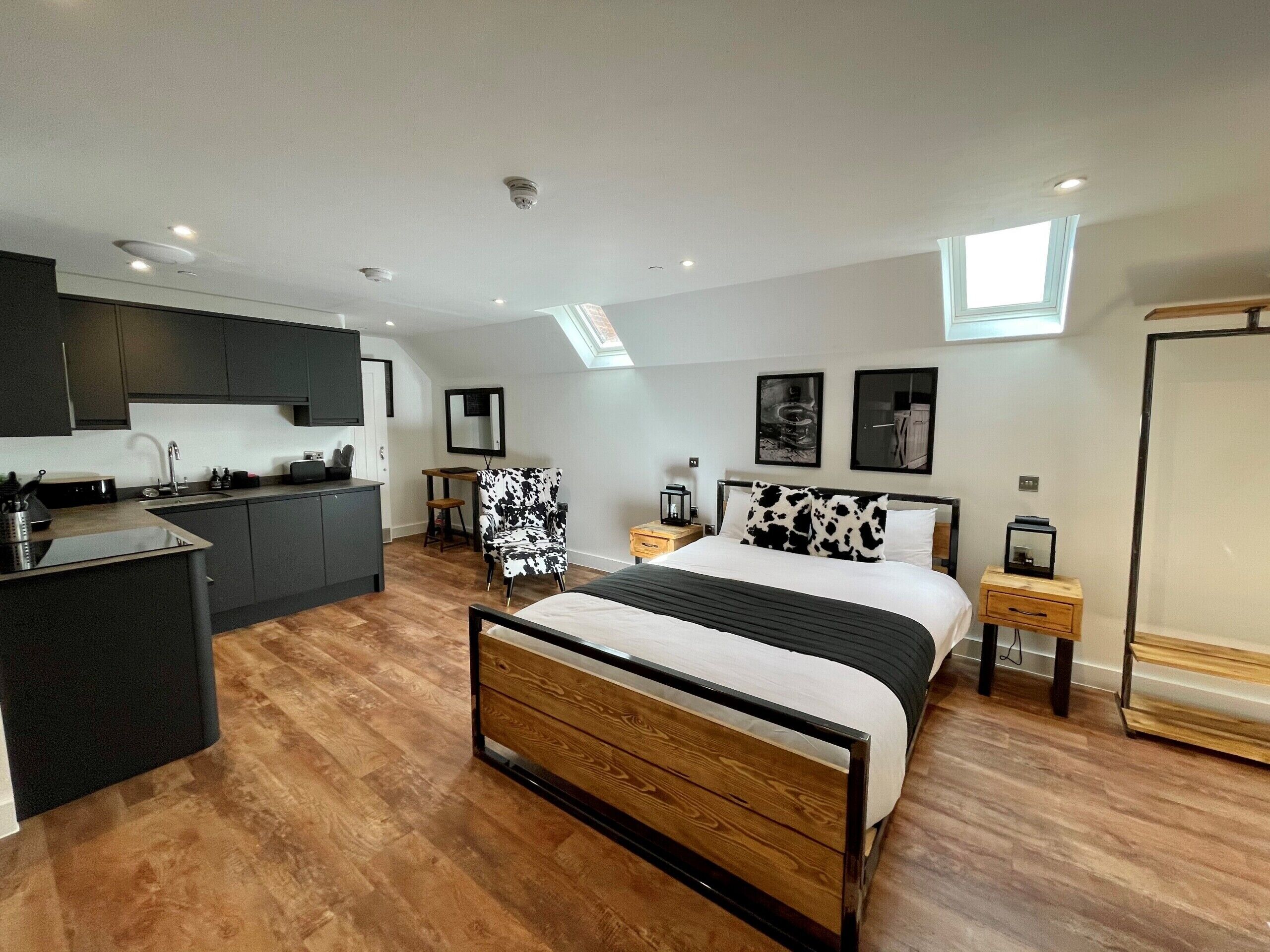 A compact bedroom with a bed, bedside tables, a chair, and a kitchenette.
