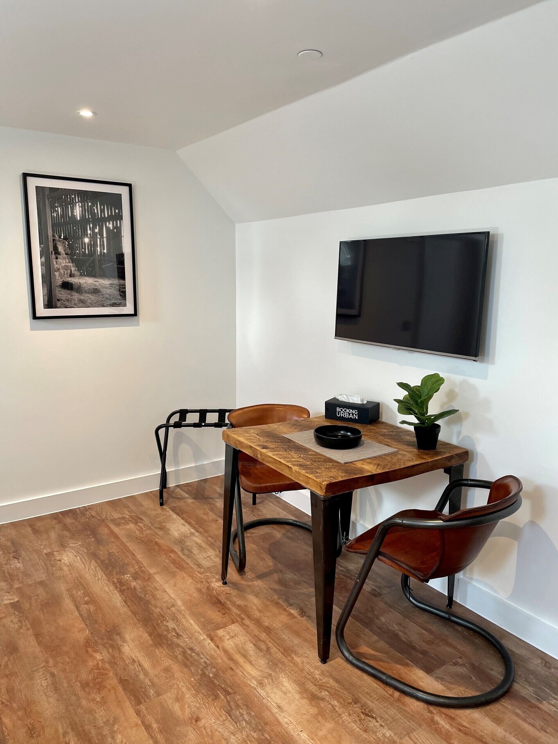 A dining area with a wooden table, two chairs, a black bowl, a potted plant, and a framed picture on the wall.