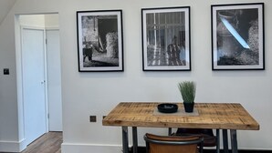 Un coin repas avec une table en bois, une plante en pot et trois photographies encadrées accrochées au mur.