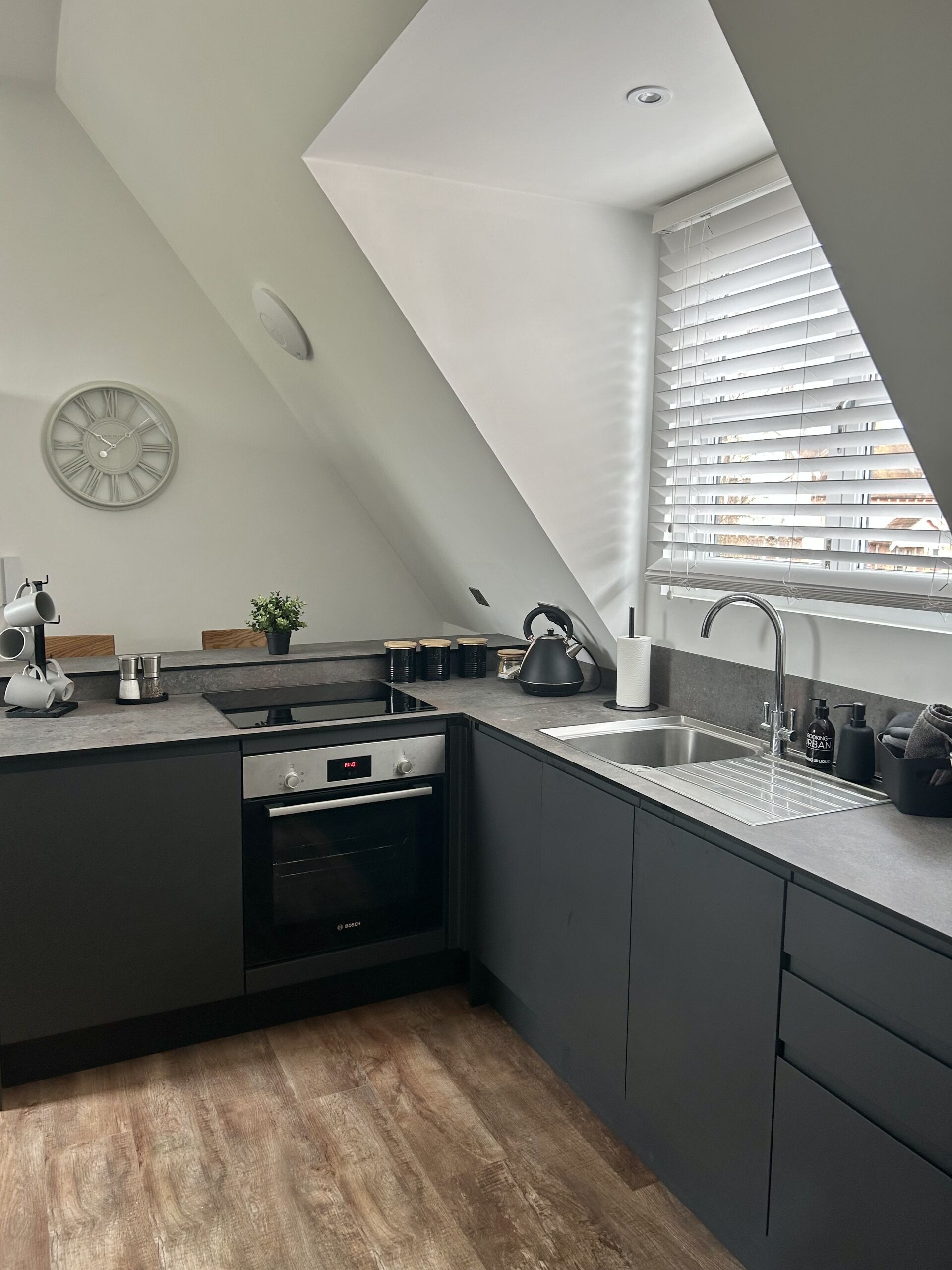 A modern kitchen with a built-in oven, a sink, and a window with blinds.