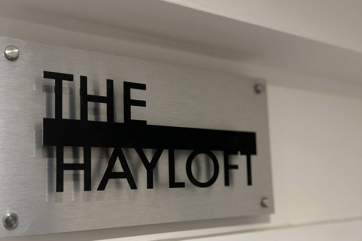 A metallic sign with the text "THE HAYLOFT" mounted on a white wall.
