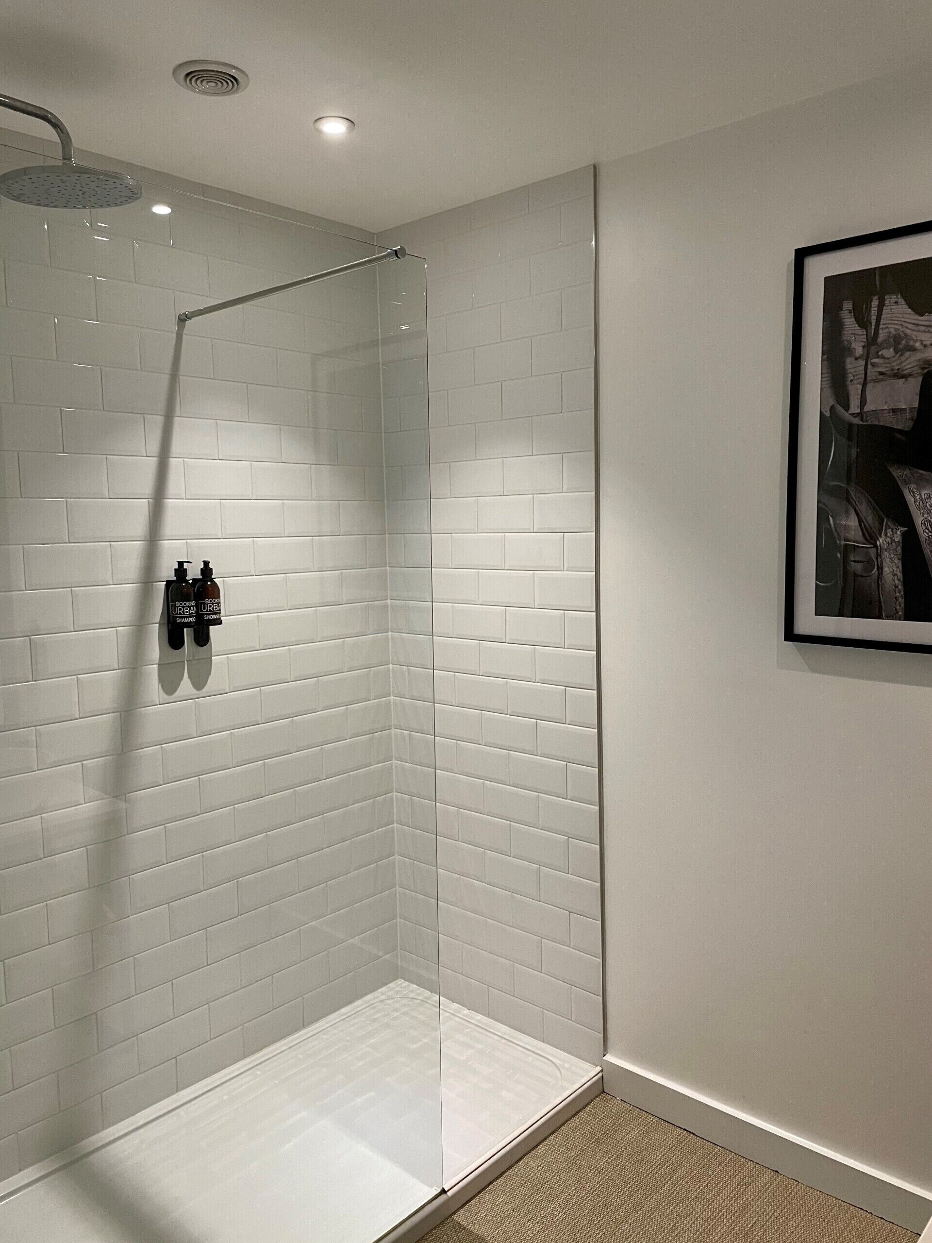 Un espace douche moderne avec des carreaux de céramique blancs de type « métro », une porte en verre et un pommeau de douche.