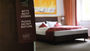 A hotel room with a bed, a red blanket, and a sign in German that says "Please do not disturb." - Landhotel Neunburg (Neunburg vorm Wald)