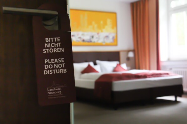 A hotel room with a bed, a red blanket, and a sign in German that says "Please do not disturb." - Landhotel Neunburg (Neunburg vorm Wald)