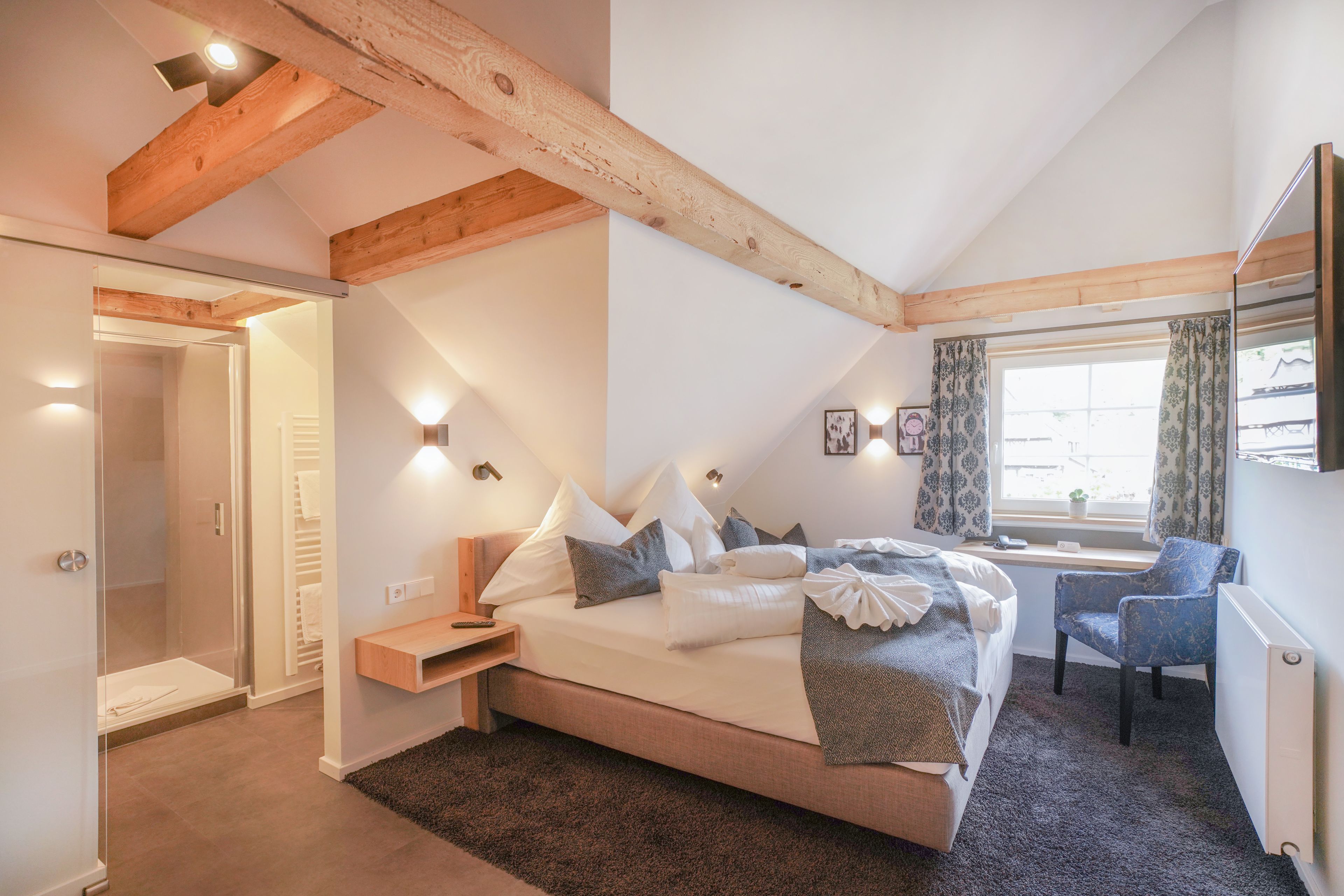 Un dormitorio con una cama grande, mesita de noche, silla y una ventana con cortinas.