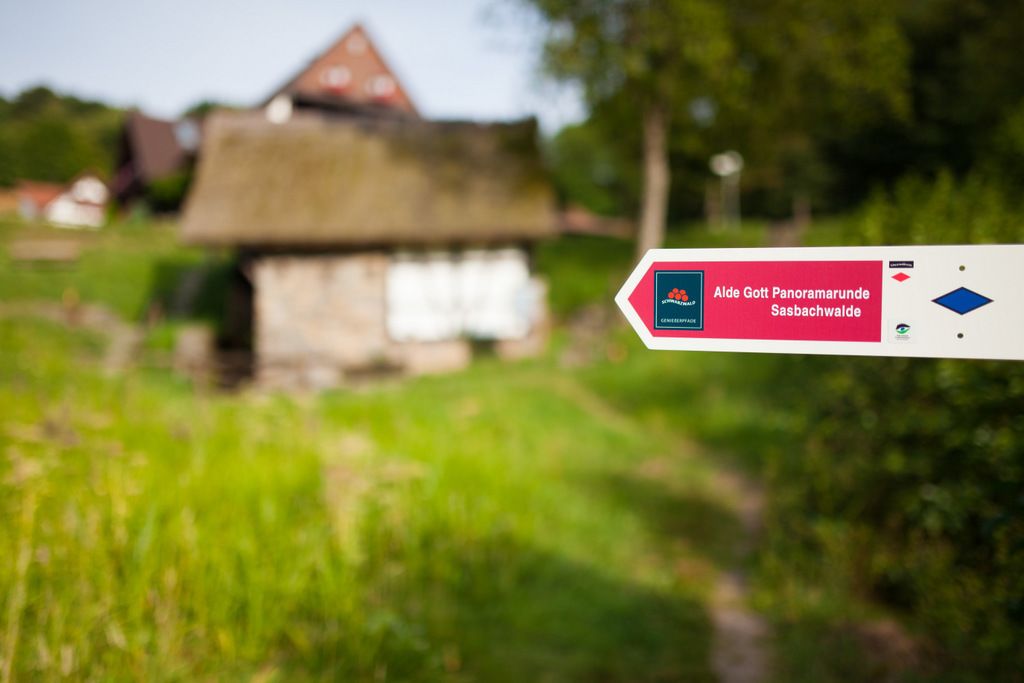 Ein Schild, das in Richtung 'Alde Gott Panoramabunde Sasbachwalde' weist, mit rotem Logo und blauem Diamant-Symbol.