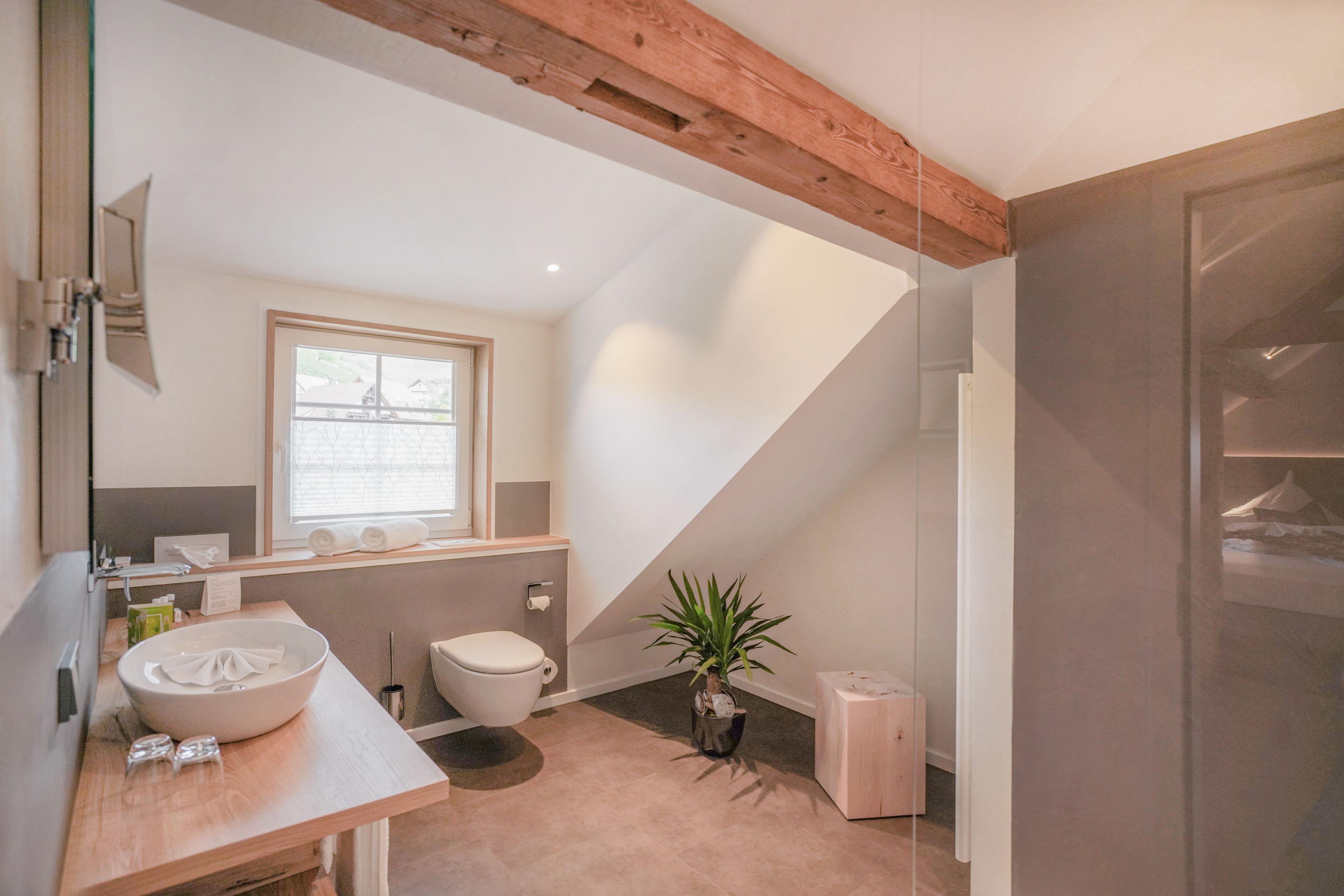 A modern bathroom with a wooden ceiling, a large sink, a toilet, and a window providing natural light.