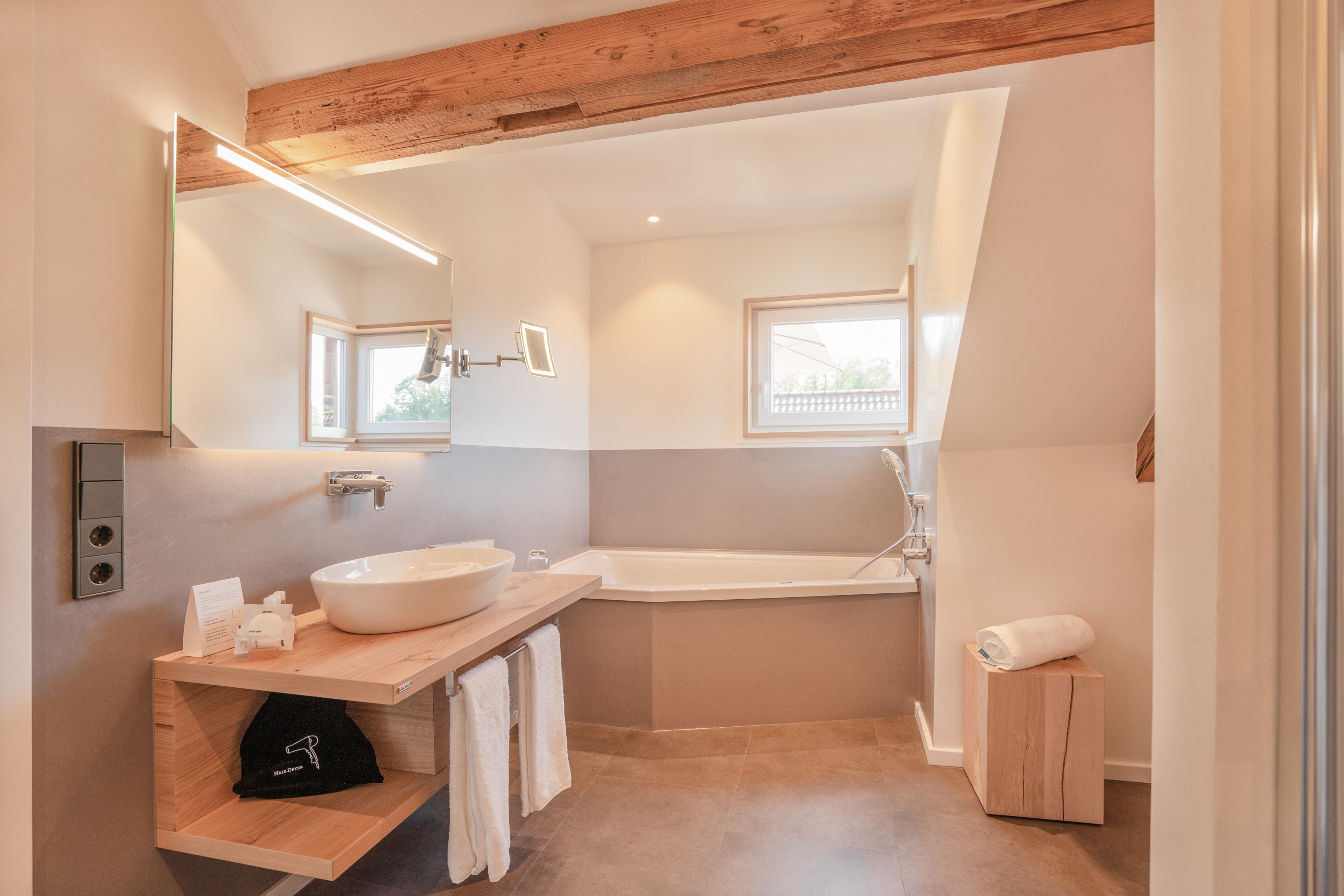 Un baño moderno con una bañera grande, un tocador de madera con lavabo y un espejo.