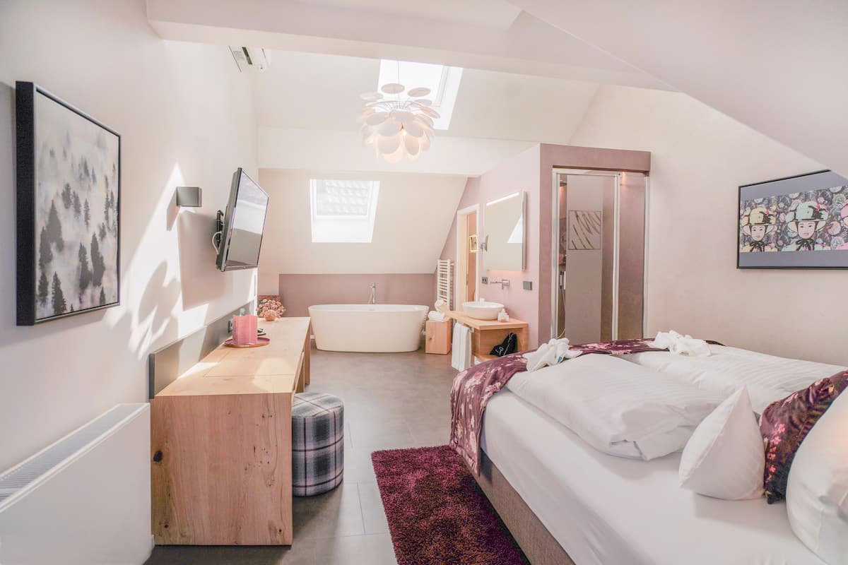 Un dormitorio con cama, escritorio, espejo, ventana y baño con bañera.