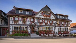 A traditional half-timbered building with a red door, multiple windows, and outdoor seating area with white chairs. - Hotel Engel (Sasbachwalden)