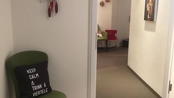 Un pasillo con una silla verde, un reloj de cuco y un cuadro en la pared.