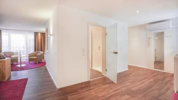 Quarto de hotel moderno com piso de madeira, um espelho grande, uma porta para o banheiro e uma área de estar com mesa e cadeiras.