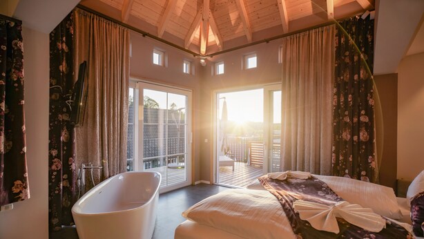 A bedroom with a large bed, a bathtub, and a balcony with a view. - Hotel Engel (Sasbachwalden)