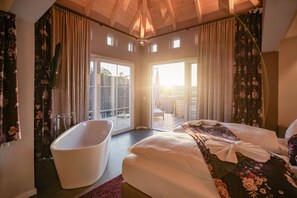 A bedroom with a large bed, a bathtub, and a balcony with a view. - Hotel Engel (Sasbachwalden)