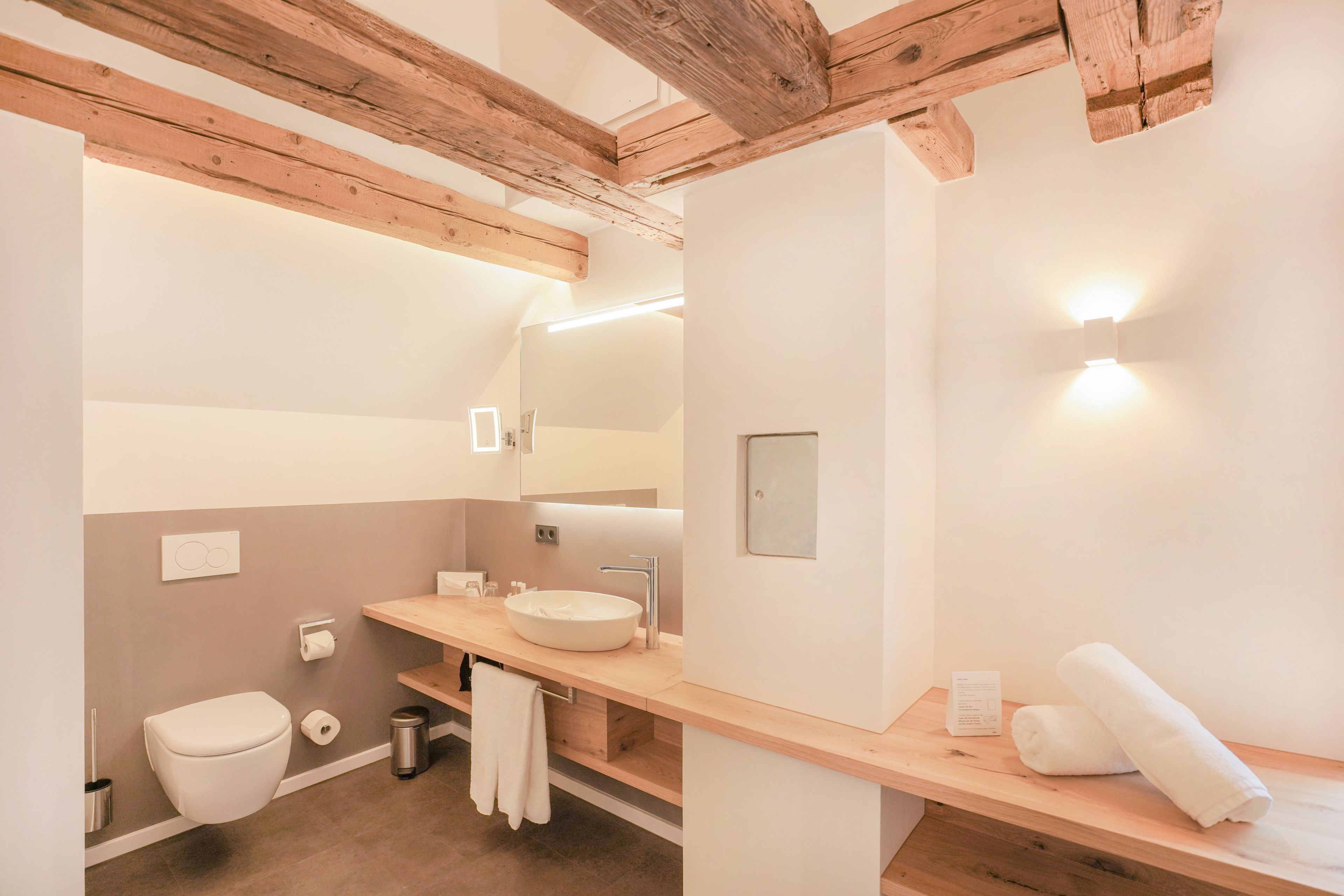 A modern bathroom with a wooden ceiling, a white sink, a mirror, and a towel on the counter.