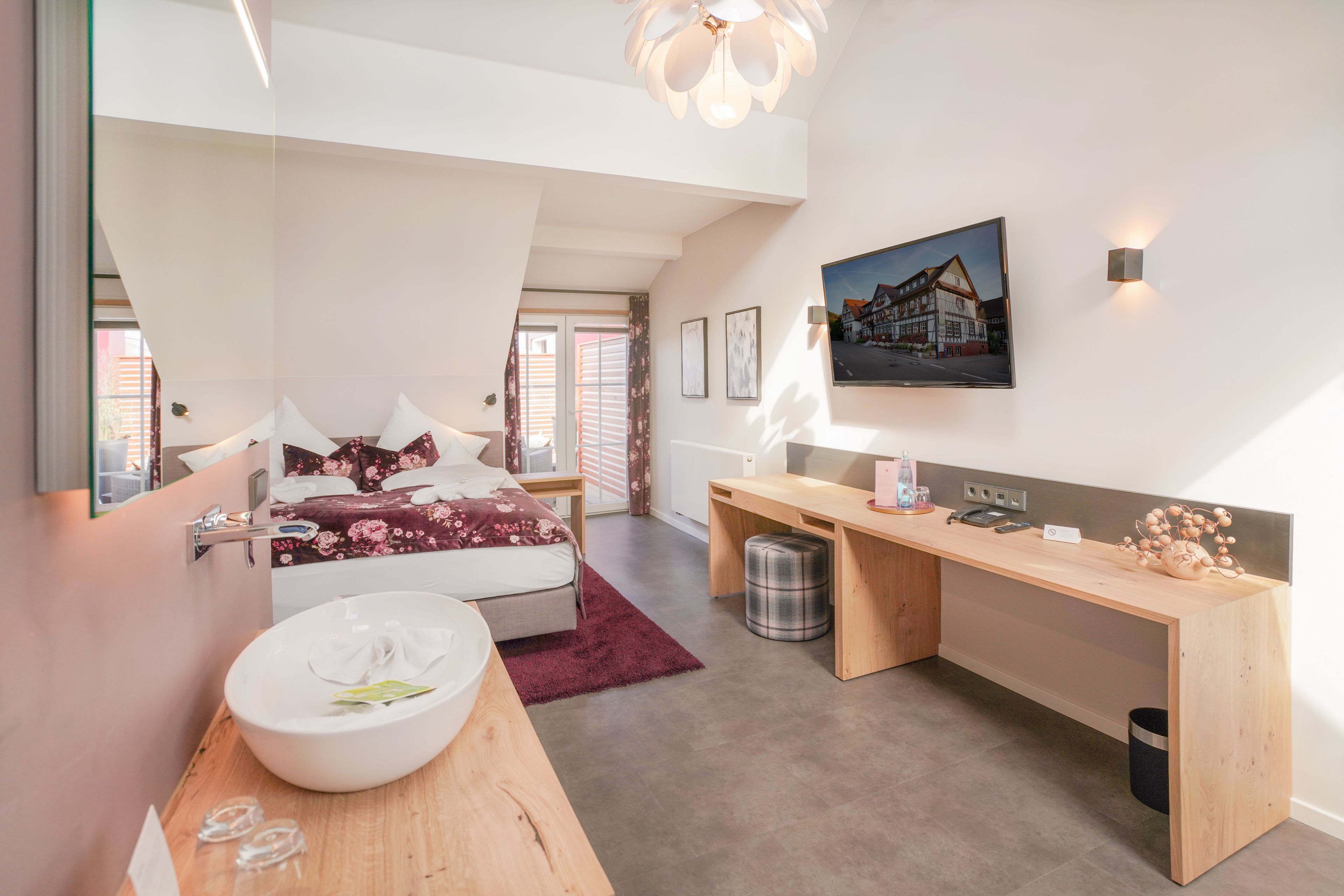 Een moderne slaapkamer met een bed, nachtkastje en een grote spiegel. Er staat een bureau met een stoel en een kleine prullenbak.