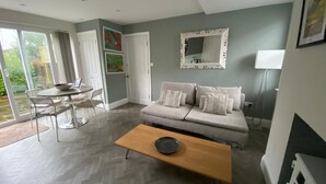 Ein modernes Wohnzimmer mit Fischgrätparkett, einer Couch mit Kissen, einem Holztisch und einem Essbereich mit Tisch und Stühlen.