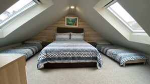 Ein Schlafzimmer mit geneigter Decke, zwei Dachfenstern, einem Bett mit gemusterten Textilien und einem gerahmten Bild an der Wand.