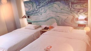 Ett hotellrum med två sängar, en vägg med marmorliknande mönster, ett skrivbord med en telefon och en lampa.